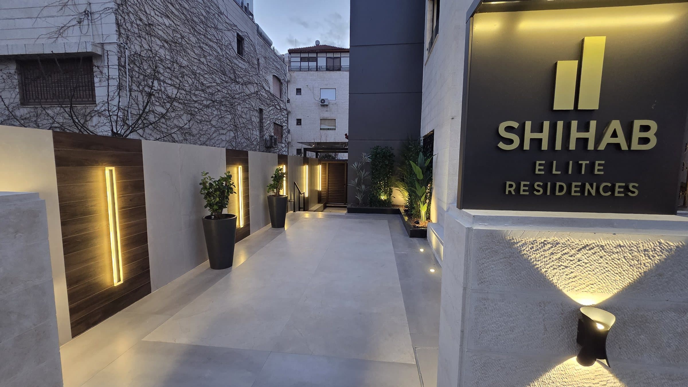 The branded SHIHAB Elite Residences arrival walkway with marble paving, integrated lighting, and planters